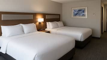 A hotel room with two beds, a nightstand, a wall-mounted lamp, and a framed picture on the wall.