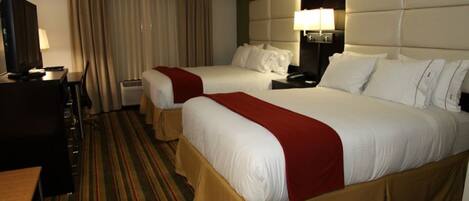 A hotel room with two beds, a desk, a lamp, and a window with curtains.