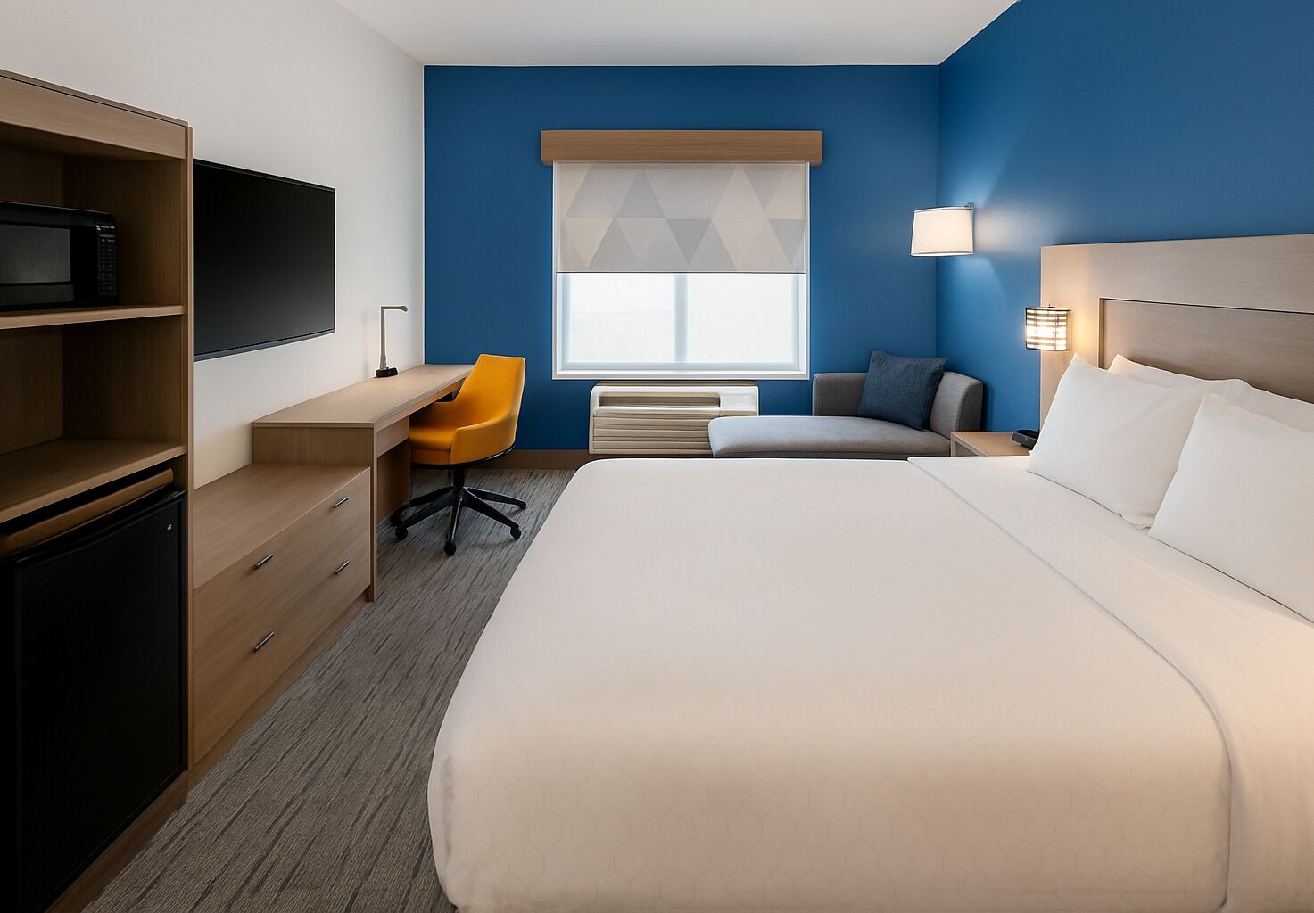 A hotel room with a bed, desk, chair, and a television.
