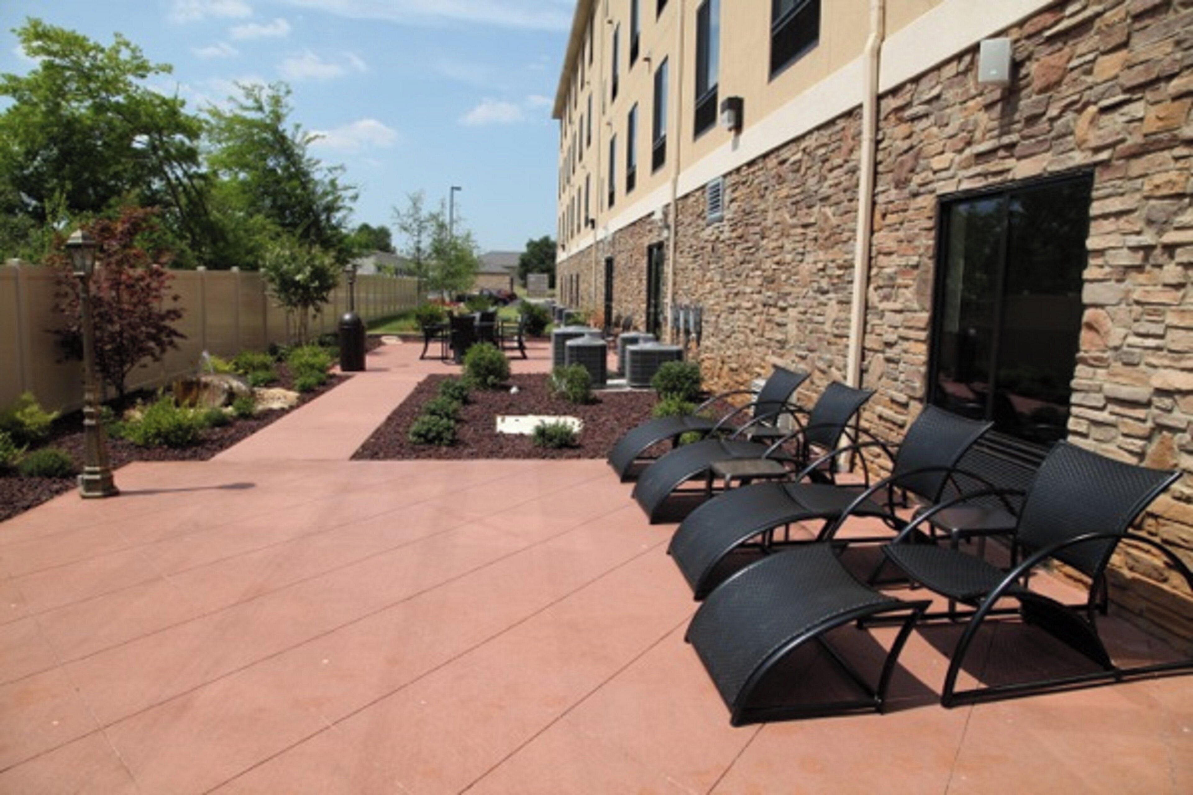 An outdoor patio area with stone walls, a paved walkway, and black metal chairs.