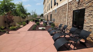 An outdoor patio area with stone walls, a paved walkway, and black metal chairs.