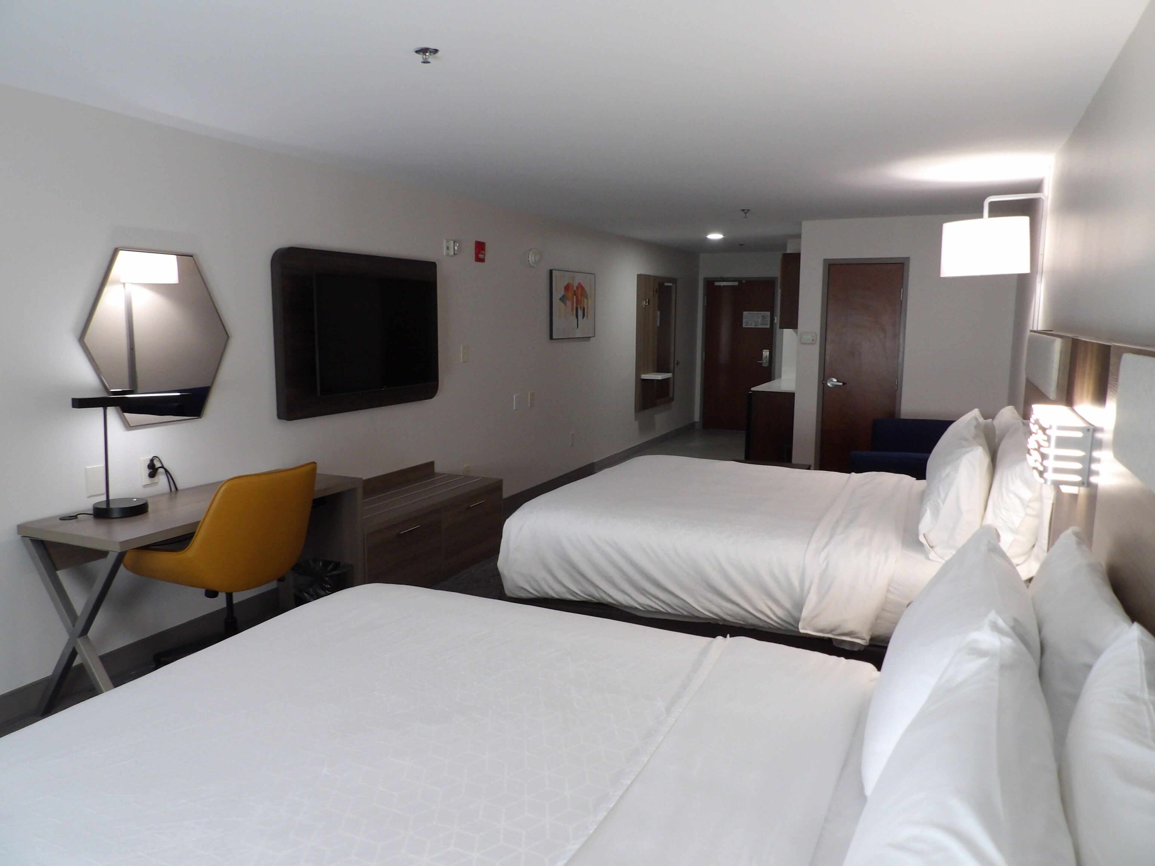 Quarto de hotel com duas camas, uma escrivaninha, uma cadeira, um abajur e uma televisão.