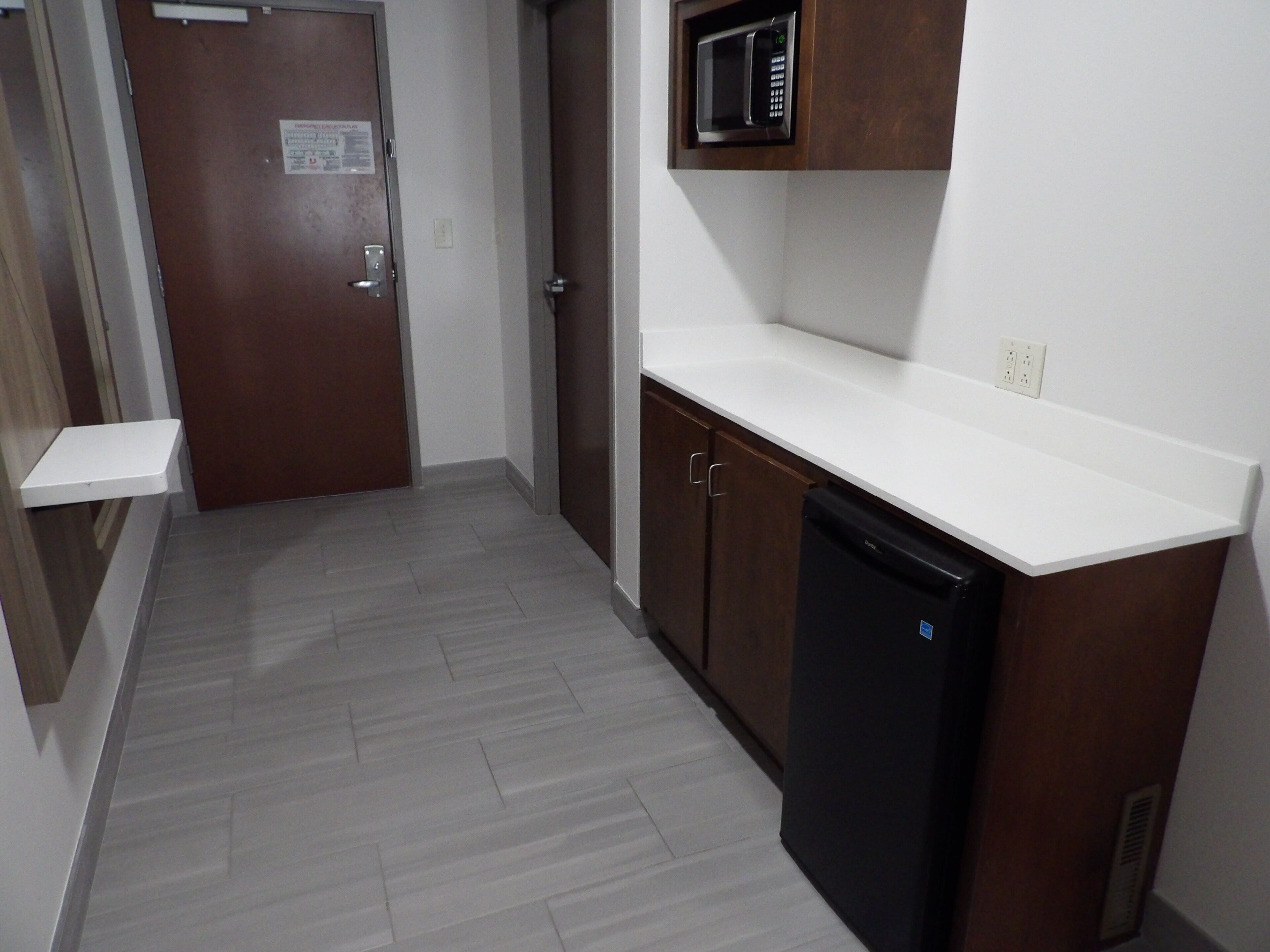 A narrow hallway with a wooden door, a microwave above a white countertop, and a black dishwasher.