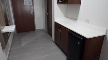 A narrow hallway with a wooden door, a microwave above a white countertop, and a black dishwasher.