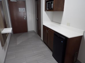 Un pasillo estrecho con una puerta de madera, un microondas sobre una encimera blanca y un lavavajillas negro.