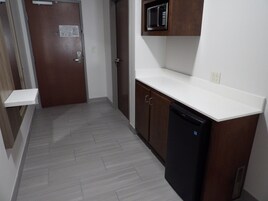 Un pasillo estrecho con una puerta de madera, un microondas sobre una encimera blanca y un lavavajillas negro.