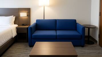 A hotel room with a bed, a blue sofa, a wooden coffee table, a nightstand, a lamp, and a small round table.