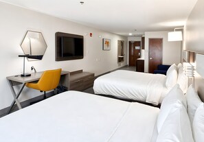 Habitación de hotel con dos camas, un escritorio con silla, televisor y baño al fondo.