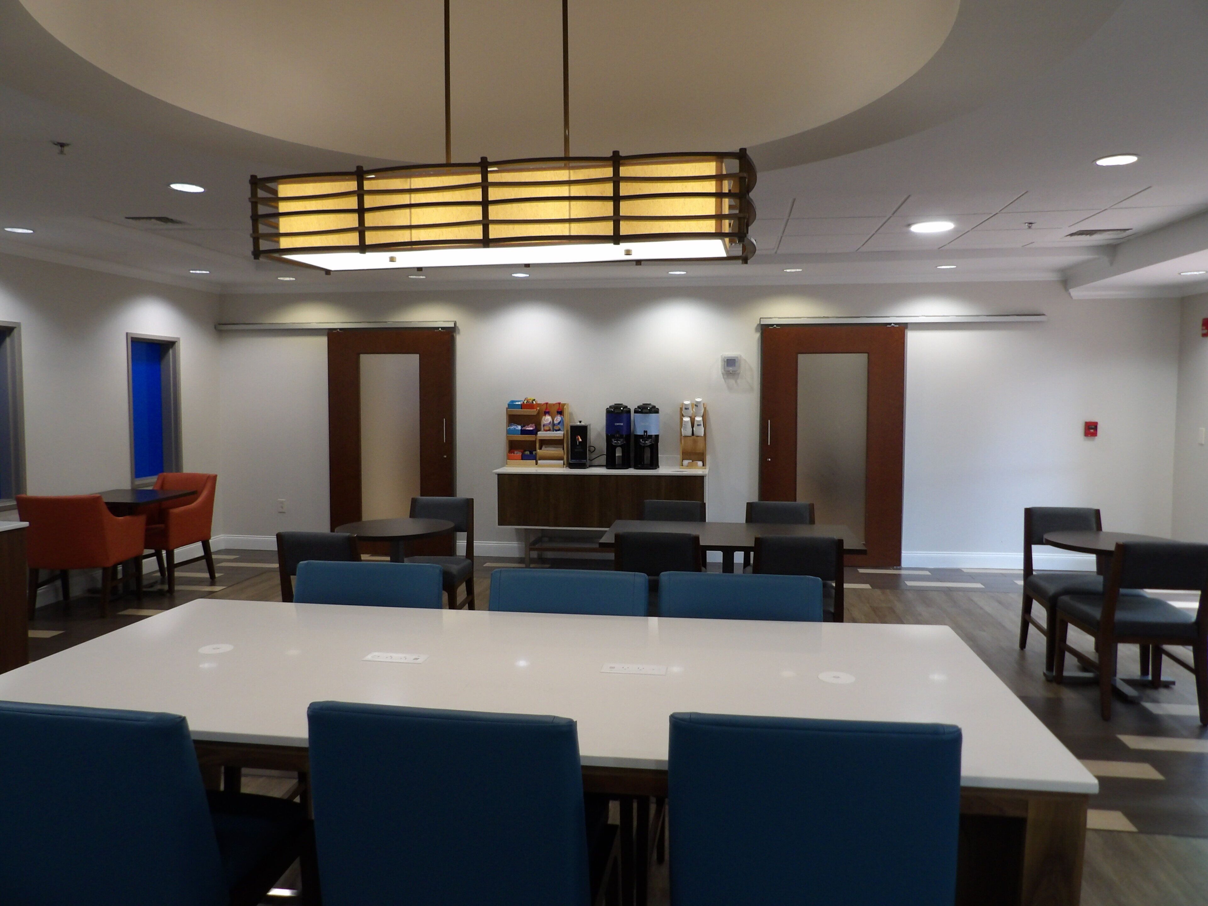A conference room with a long table, blue chairs, a coffee station, and a modern ceiling light fixture.