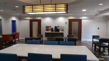 A conference room with a long table, blue chairs, a coffee station, and a modern ceiling light fixture.