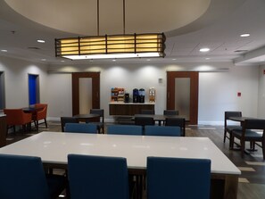 A conference room with a long table, blue chairs, a coffee station, and a modern ceiling light fixture. - Holiday Inn Express & Suites Huntsville Airport by IHG (Madison)