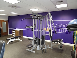 Un gimnasio con equipo de ejercicio, una banca y una pared con el texto "100 AHEAD FLEXABLE".