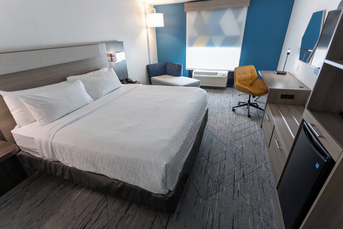 Habitación de hotel con una cama grande, un escritorio, una silla, una lámpara de escritorio, un aire acondicionado y una televisión.
