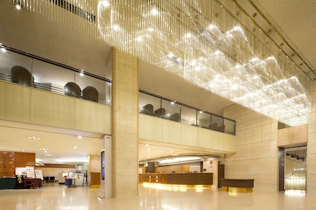 A spacious lobby with a modern design, featuring a reception desk, seating area, and a high ceiling with decorative lighting.