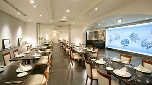 A spacious dining area with long tables set for multiple guests, featuring a modern chandelier and a decorative wall with floral patterns. - Castle Plaza Hotel (Nagoya)