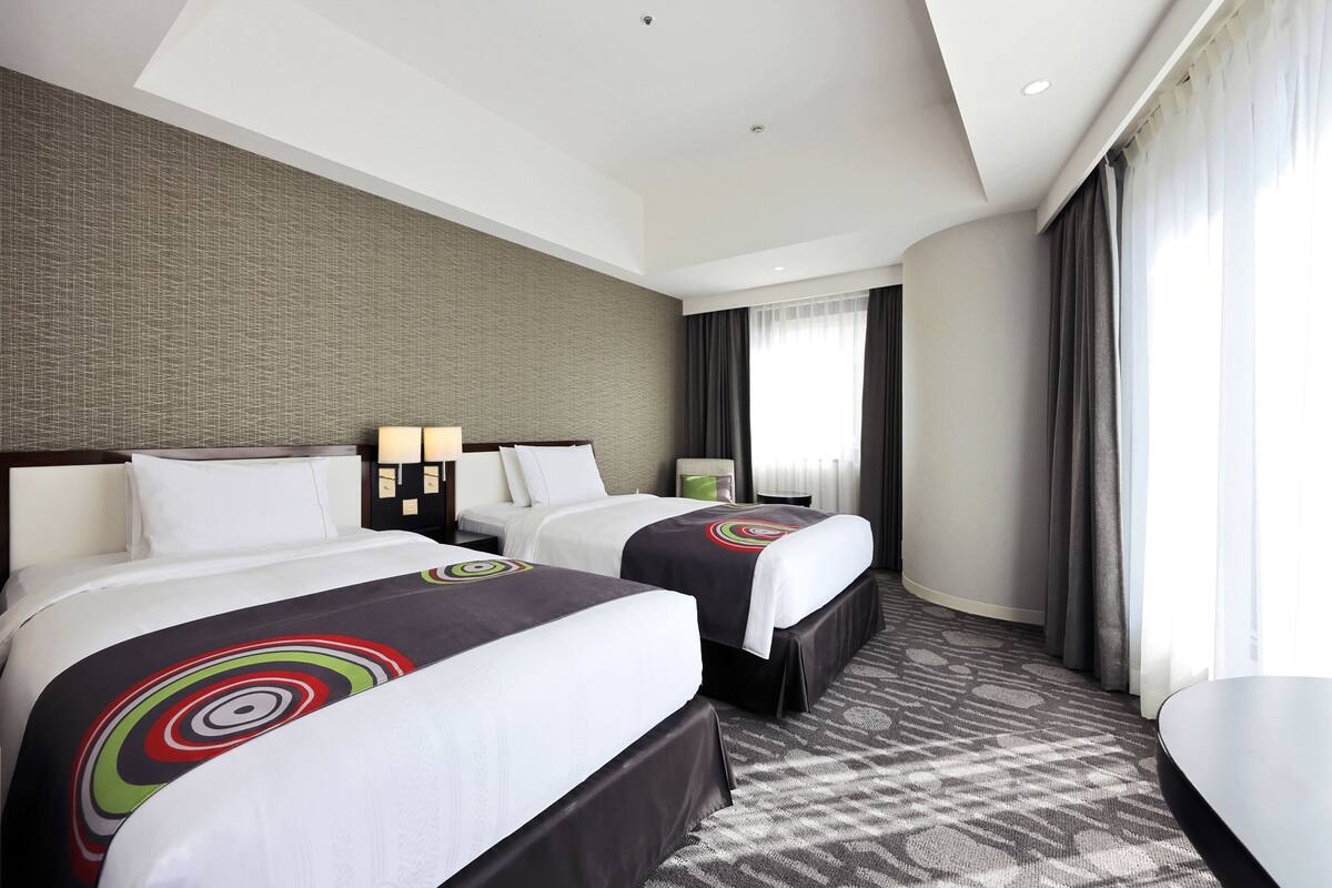 Ein Hotelzimmer mit zwei Betten, einem großen Fenster mit Vorhängen, einem gemusterten Teppich und einem modernen Decken­design.