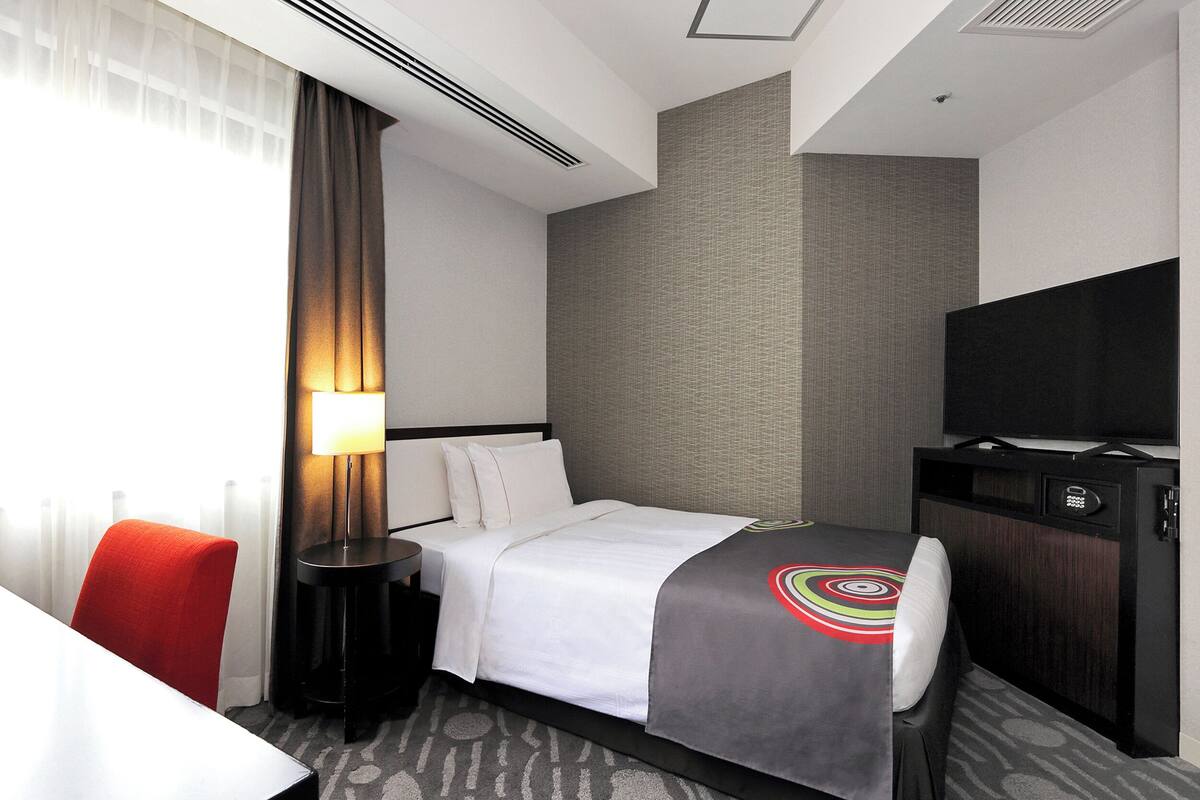 Ein Hotelzimmer mit Bett, Fernseher, Schreibtisch und Stuhl.