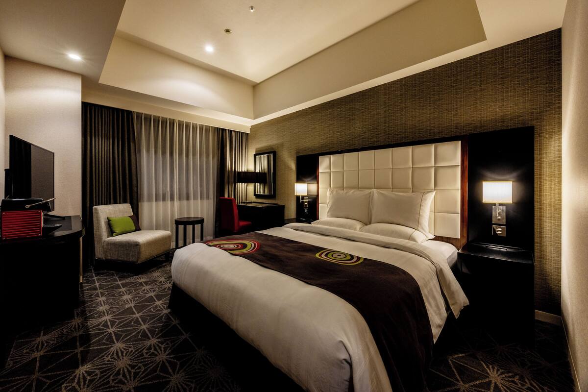 Ein Hotelzimmer mit einem großen Bett, einem Schreibtisch, einem Stuhl, einem Fernseher und einem Fenster mit Vorhängen.