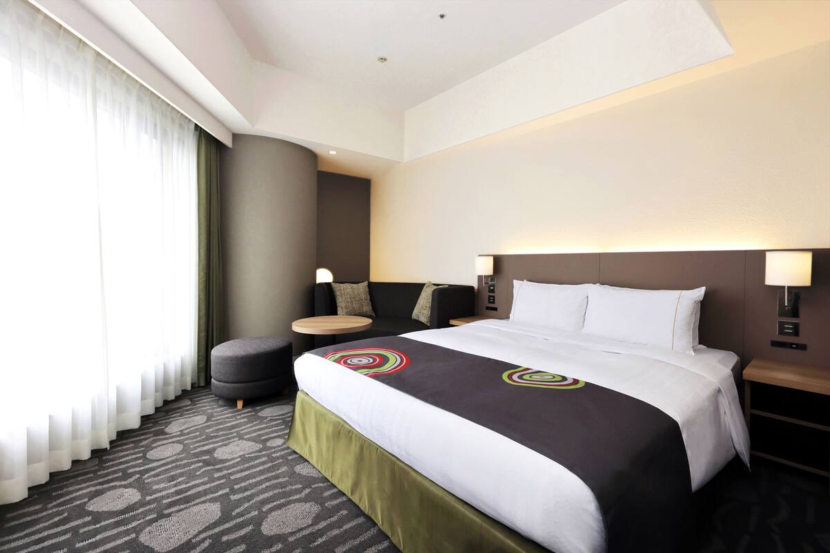 Ein Hotelzimmer mit einem großen Bett, einer kleinen Couch, einem runden Tisch und einer Lampe.