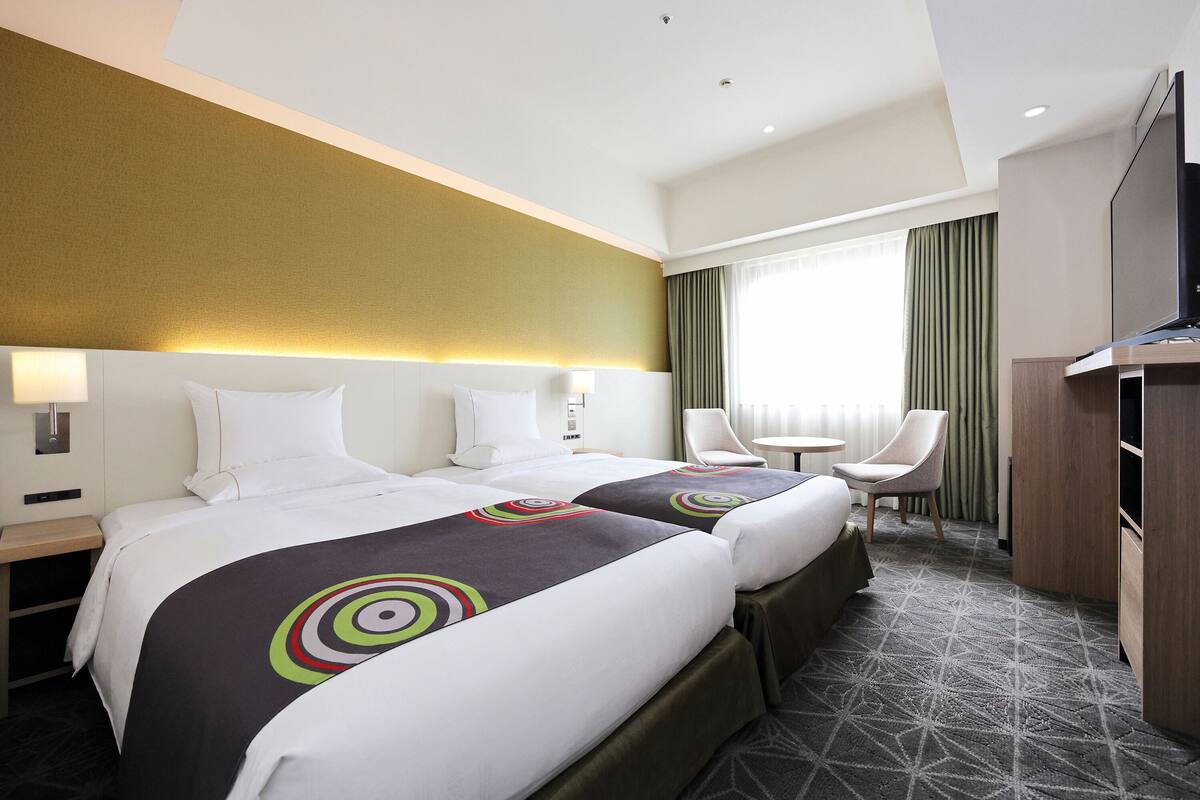 Ein Hotelzimmer mit zwei Betten, einem Fernseher, einem Schreibtisch und einem Stuhl.