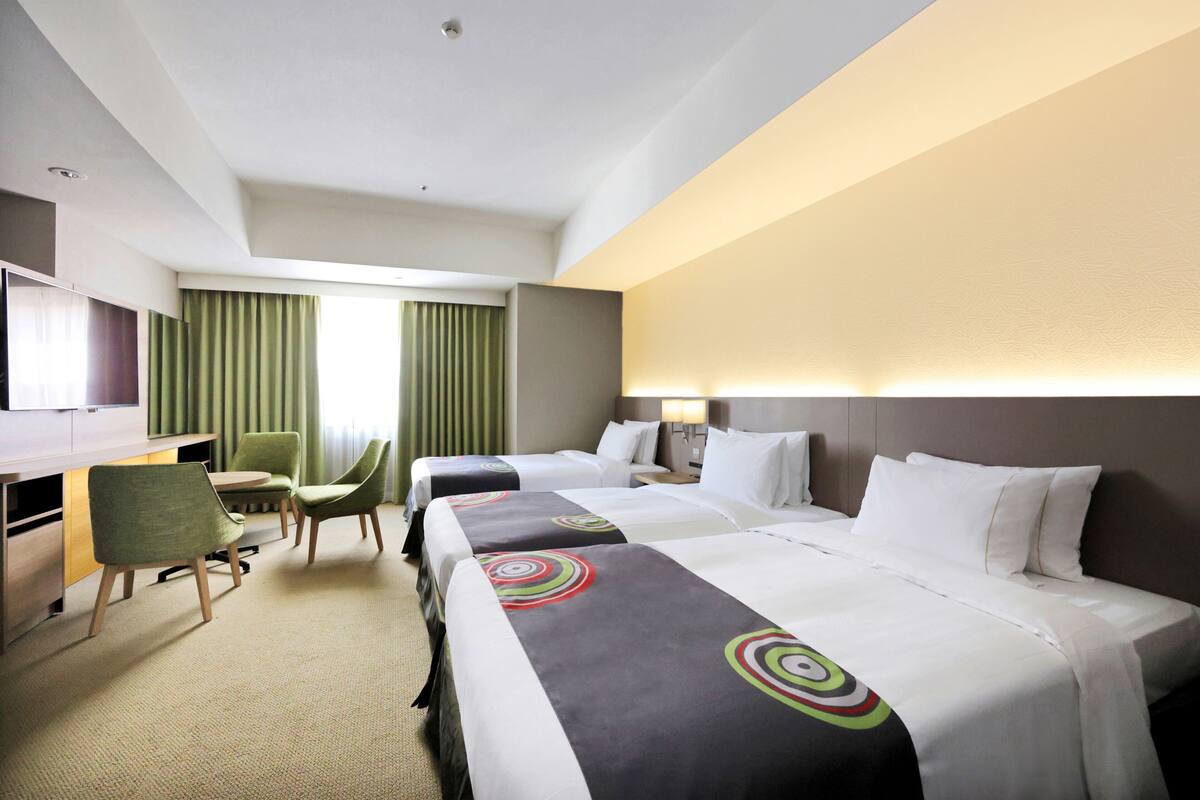 Ein Hotelzimmer mit zwei Betten, einem Schreibtisch, einem Sessel und einem Fernseher.