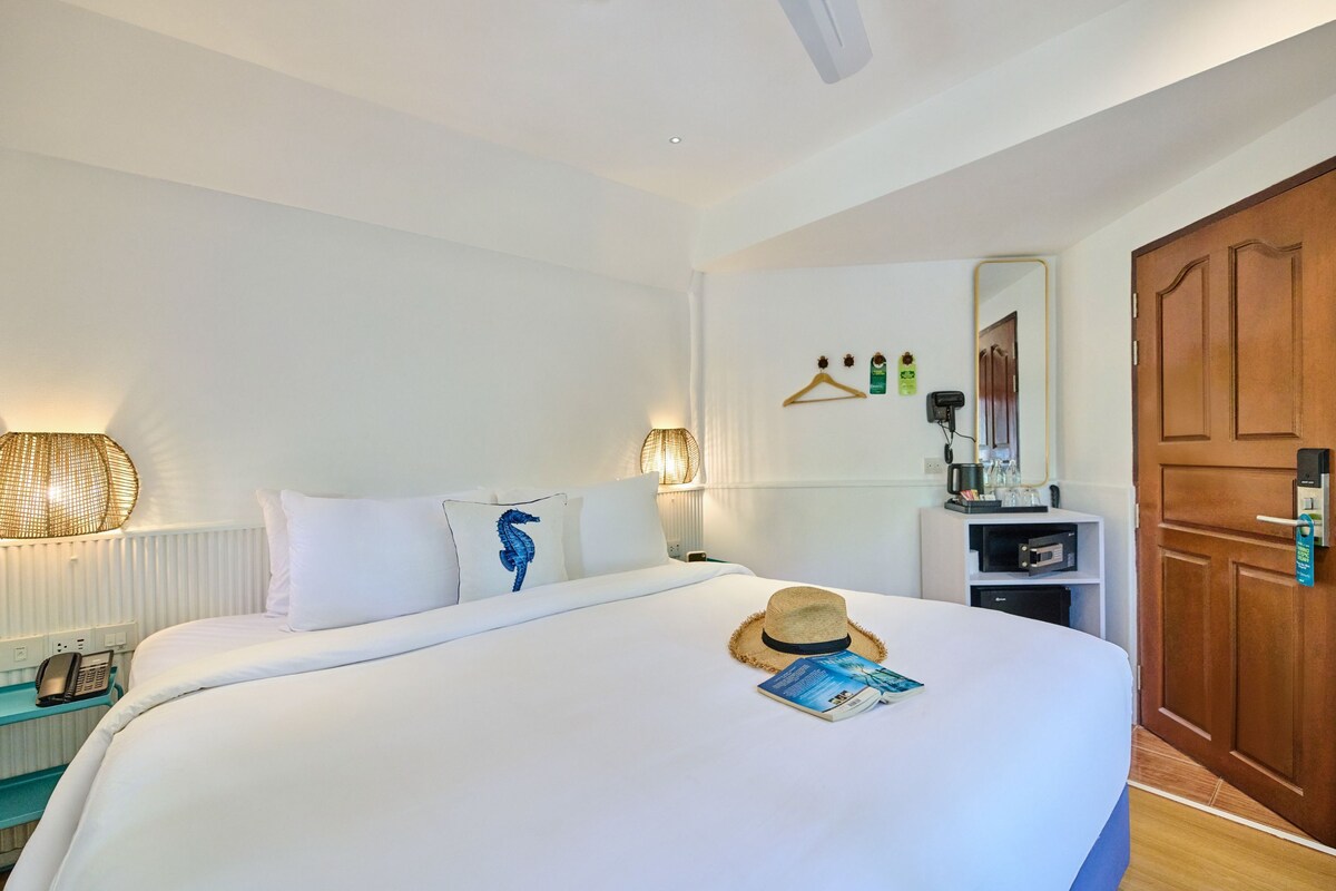 A hotel room with a bed, a bedside table with a lamp, a mirror, a wardrobe, and a door.
