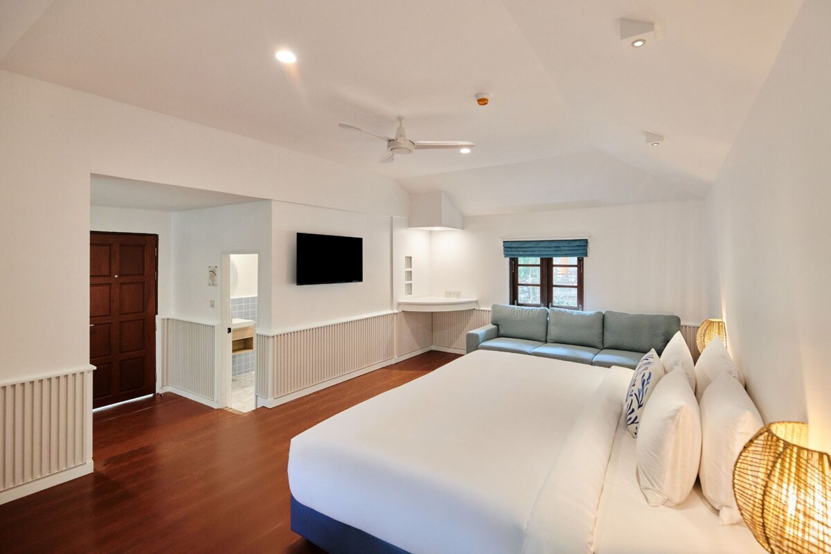 Un dormitorio con una cama grande, un televisor montado en la pared, un ventilador de techo y una ventana con vistas.