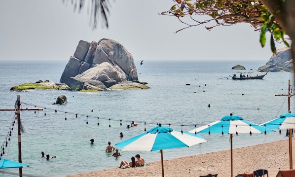 A beach with umbrellas and people swimming.