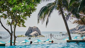 A pool area with umbrellas, palm trees, and a rocky outcrop in the background. -  Lub d Koh Tao Tanote Bay (Koh Tao)