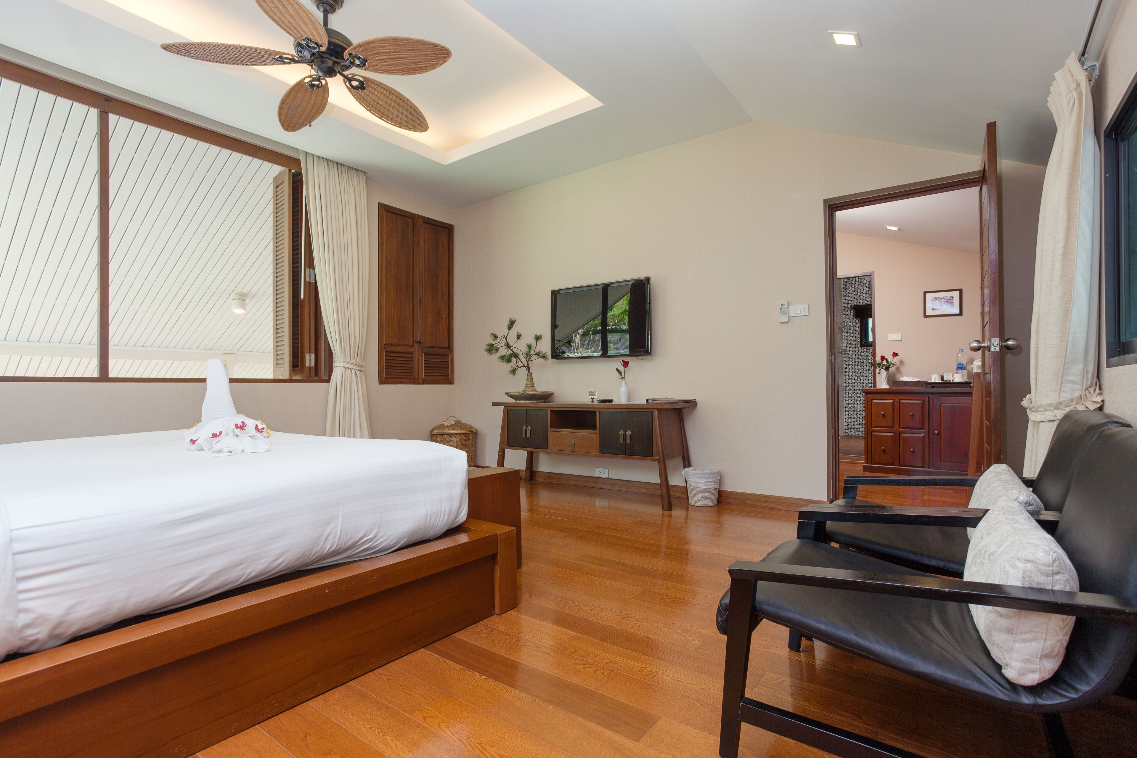 A hotel room with a bed, a desk, a chair, a ceiling fan, and a TV.