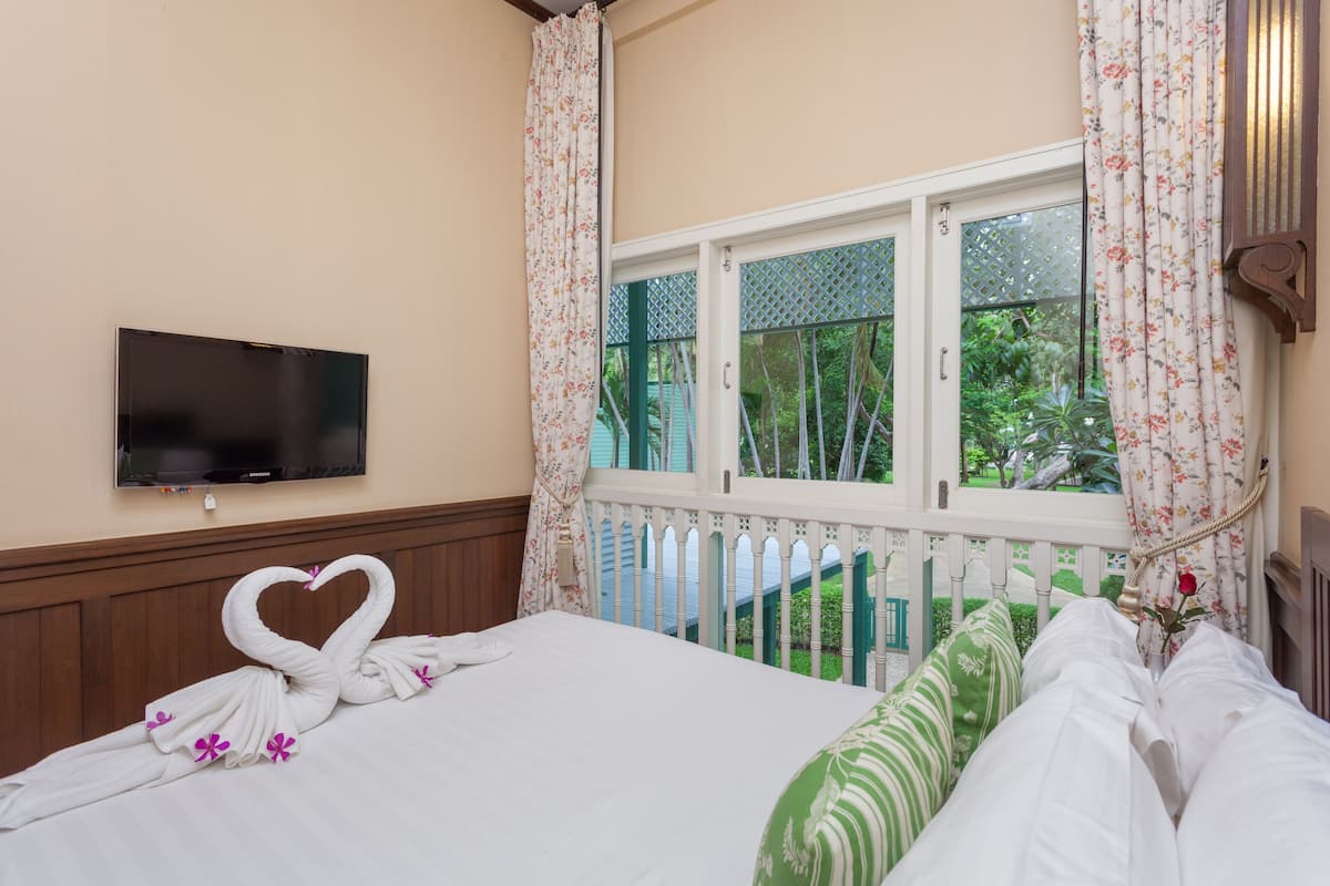 A hotel room with a bed, a TV mounted on the wall, and a window with a view of greenery.