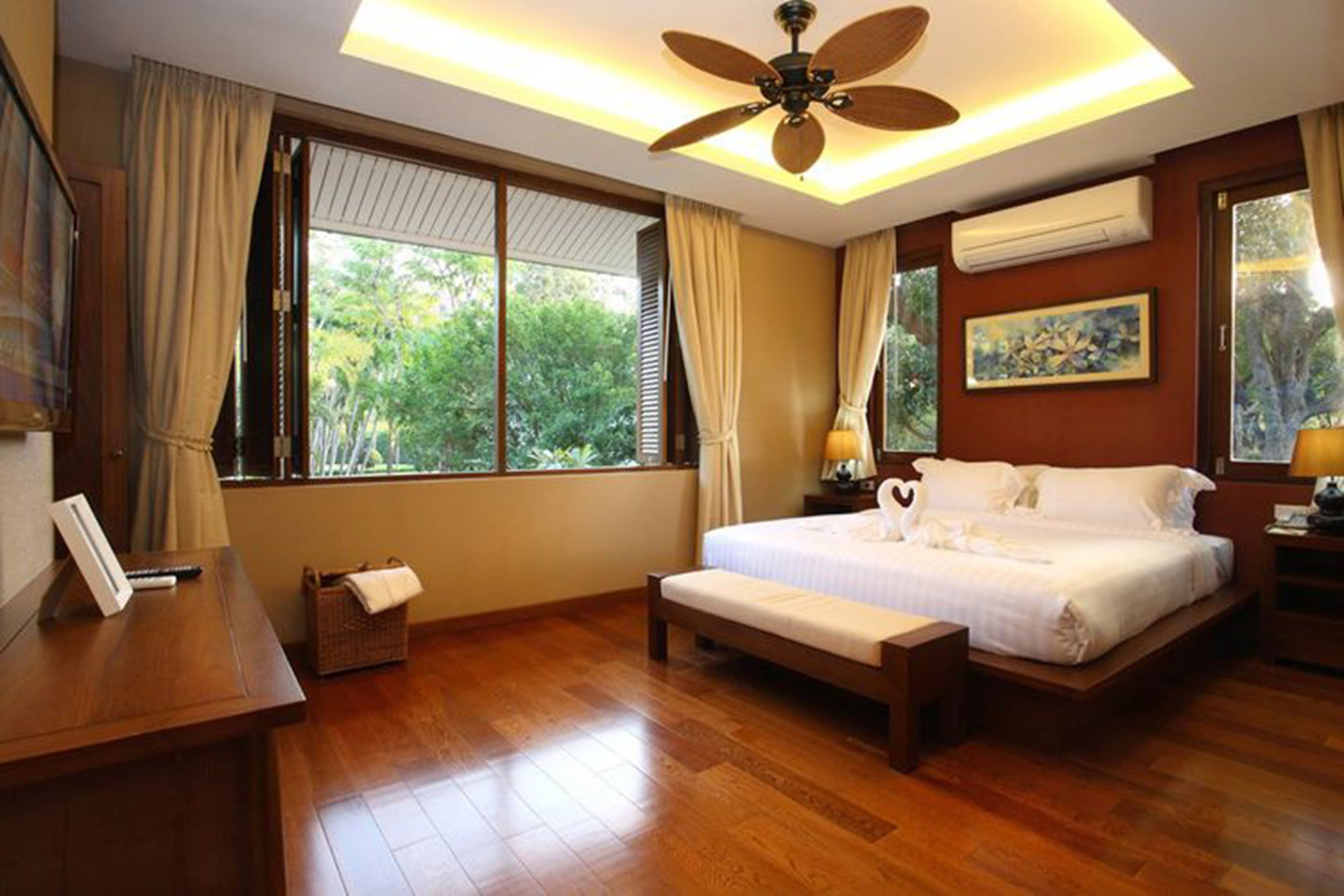 A bedroom with a large bed, a ceiling fan, and a view of greenery outside.
