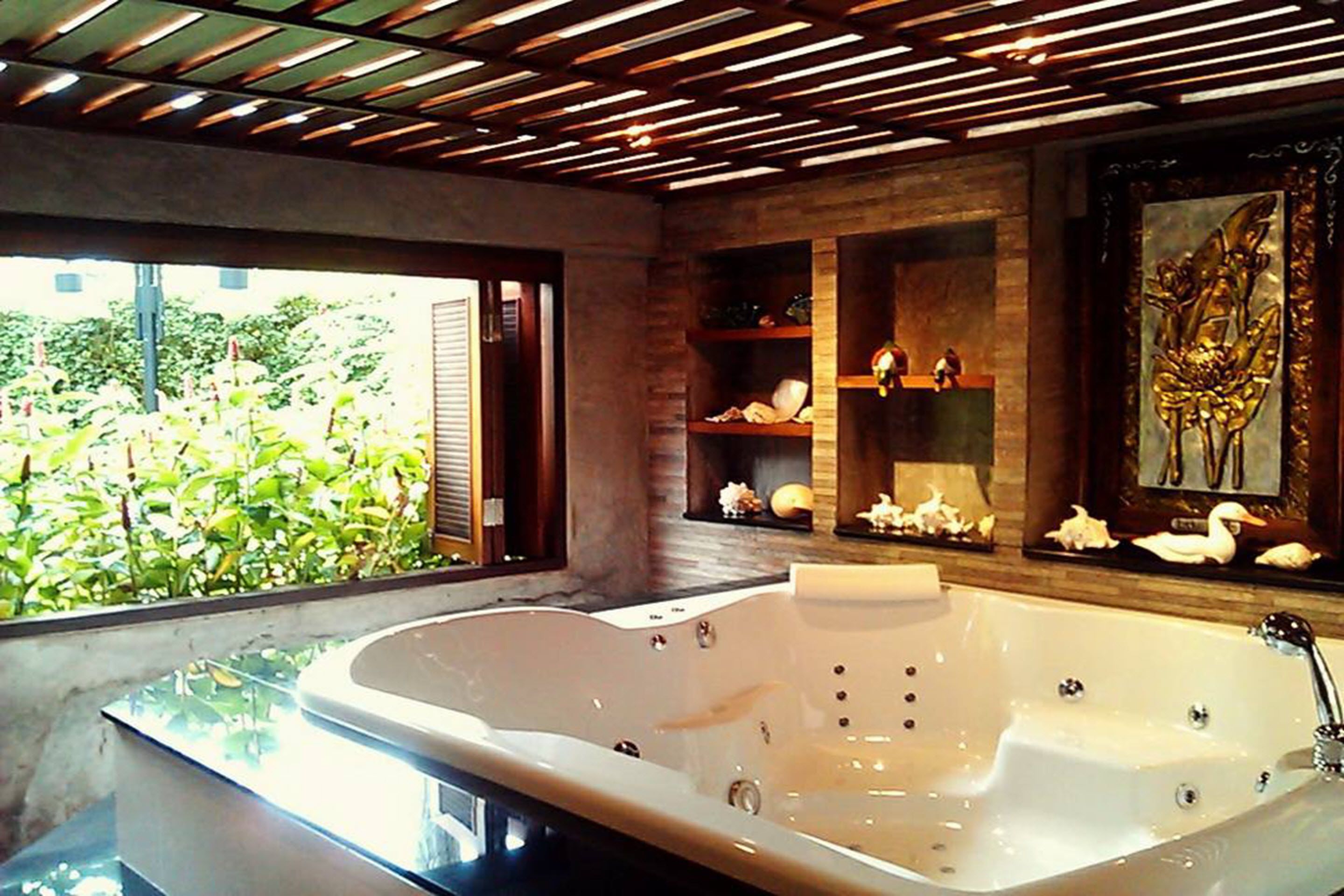 Un baño moderno con una bañera grande, estantes de madera con adornos y vistas a la vegetación.