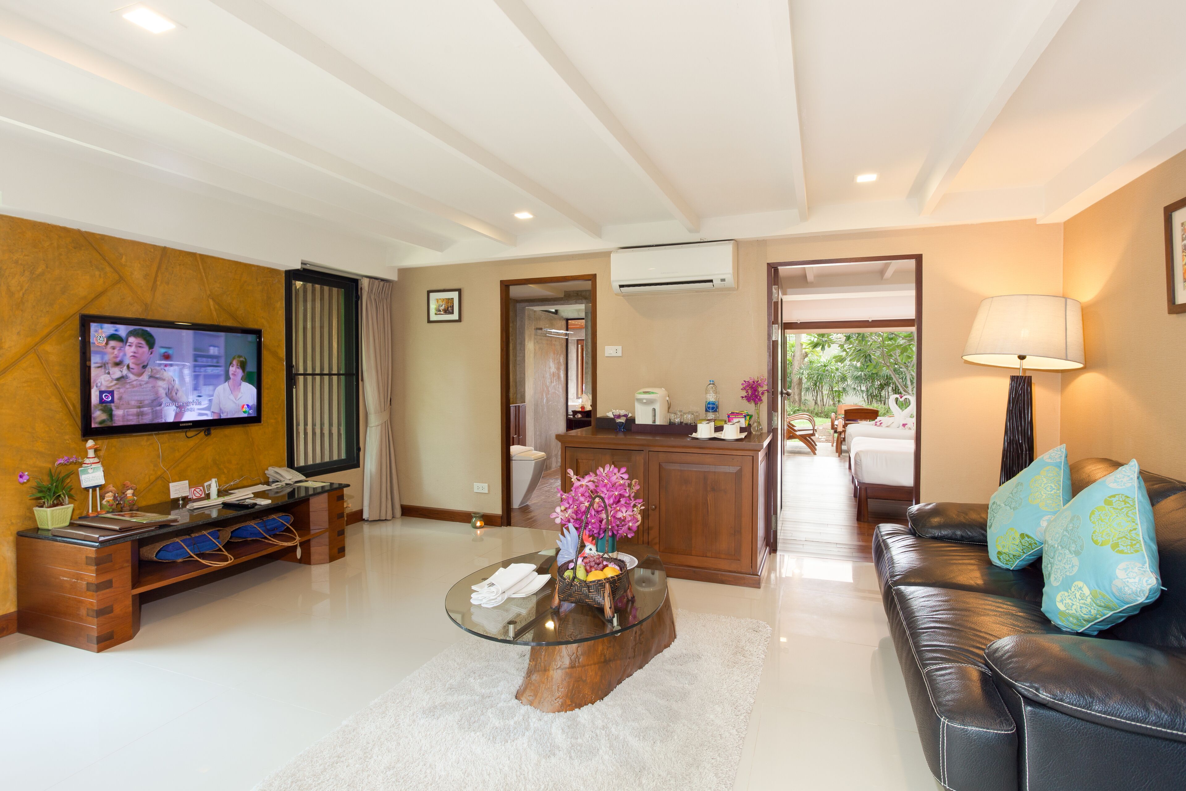 A modern living room with a flat-screen TV, a glass coffee table, a leather sofa, and a wooden reception desk.