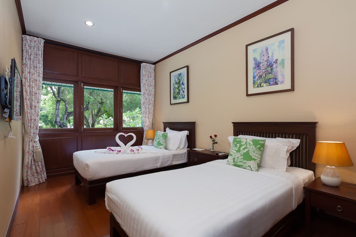 A hotel room with two beds, a window with curtains, a painting on the wall, and a lamp on the nightstand.