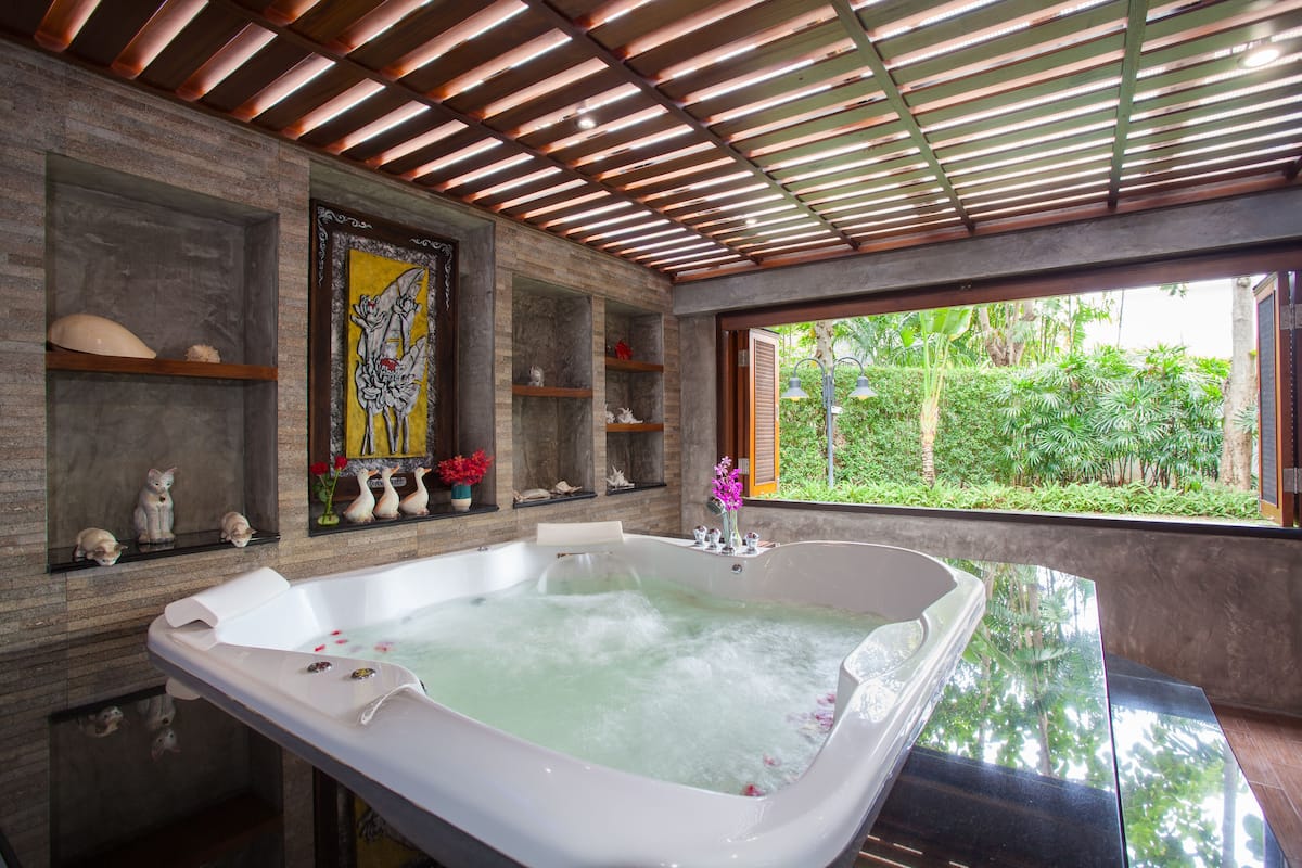 A modern bathroom with a large bathtub, wooden shelves with decorative items, and a view of lush greenery.
