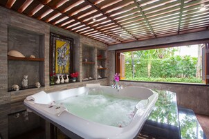 Un baño moderno con una bañera grande, estantes de madera con objetos decorativos y vistas a vegetación exuberante.