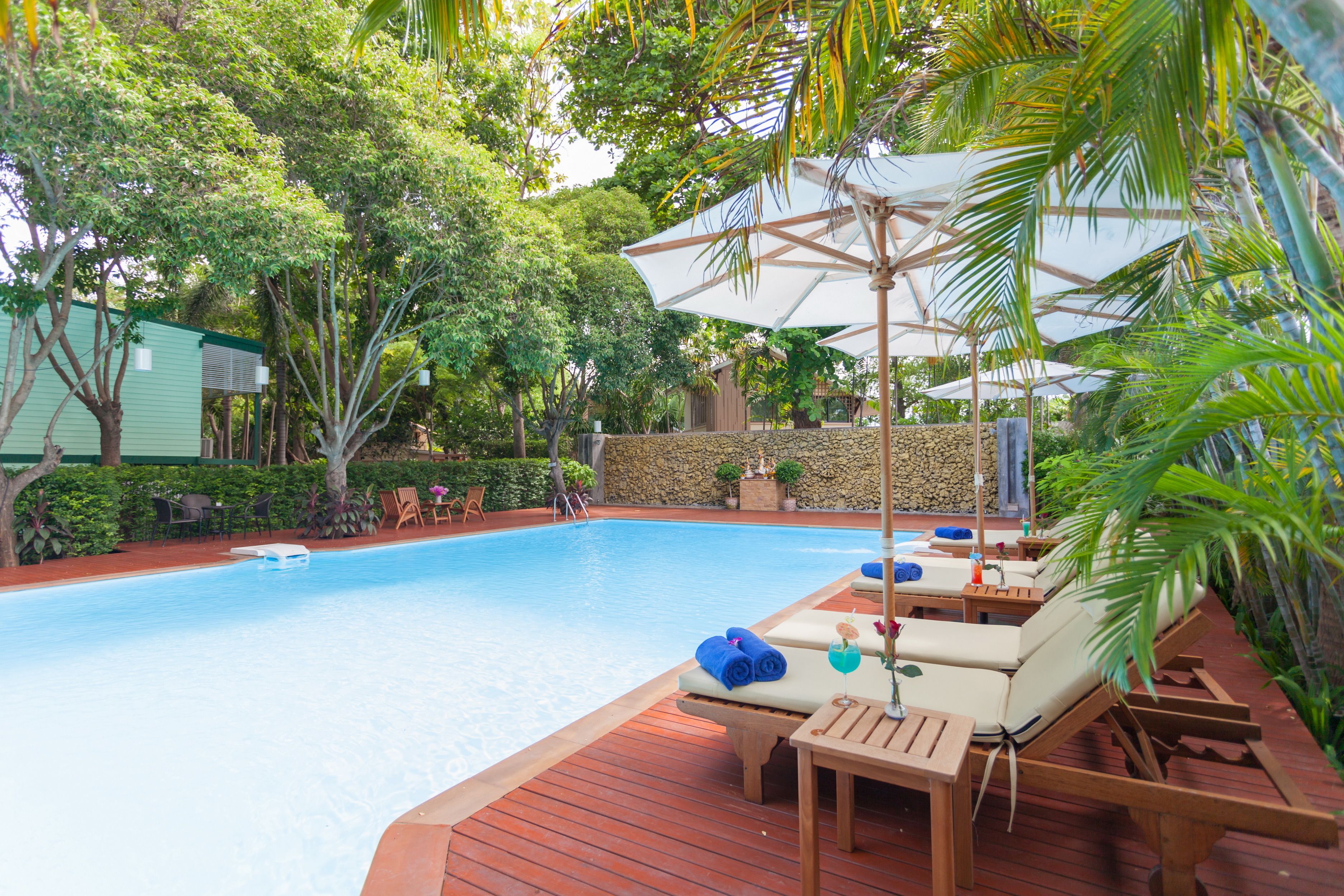 A pool area with lounge chairs and umbrellas, surrounded by greenery.