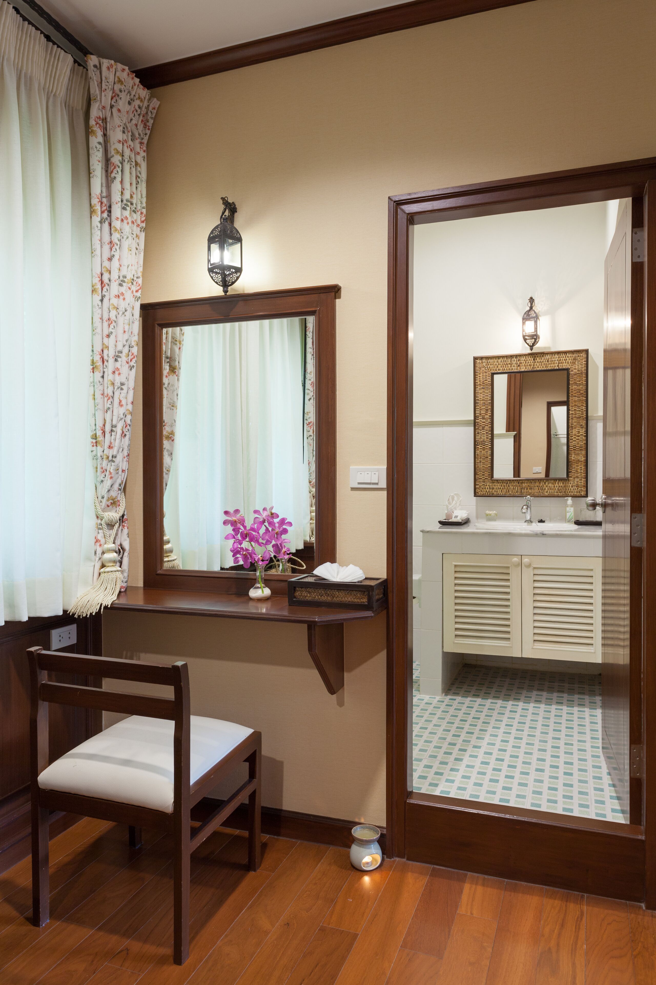 A bathroom with a wooden vanity, a mirror, a small vase with flowers, and a toilet.