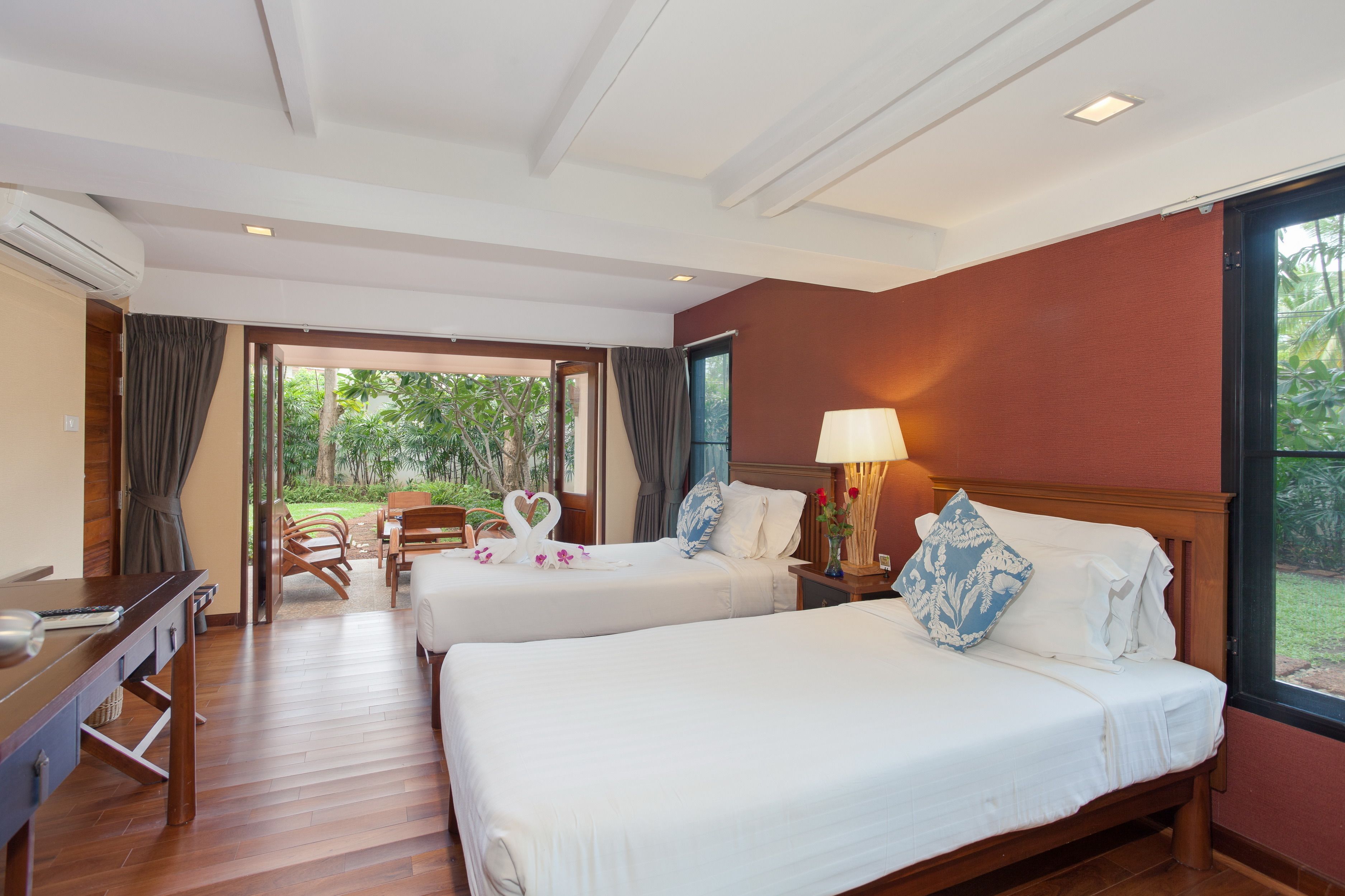 A hotel room with two beds, a desk, and a view of the garden.
