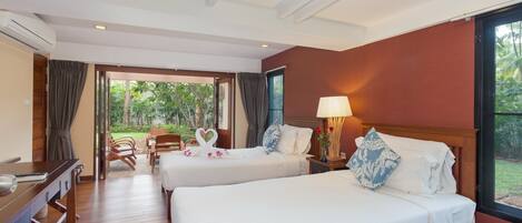 A hotel room with two beds, a desk, and a view of the garden.