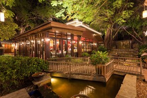 Ein traditionelles japanisches Restaurant mit Holzbauweise, einer kleinen Brücke über einem Teich und üppiger Bepflanzung rundherum.