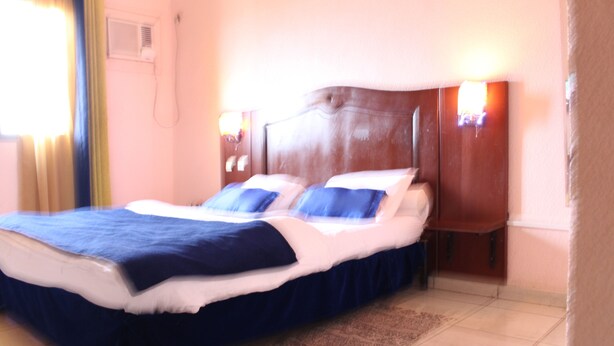 A hotel room with a large bed, two bedside tables, and a window with curtains. - Prestige Hotel (Yaoundé)