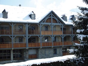 Un chalet à plusieurs étages, doté de balcons en bois et de murs en pierre, entouré de neige.