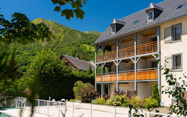 Un immeuble à plusieurs étages doté de balcons, d’une piscine et surplombant un paysage montagneux.