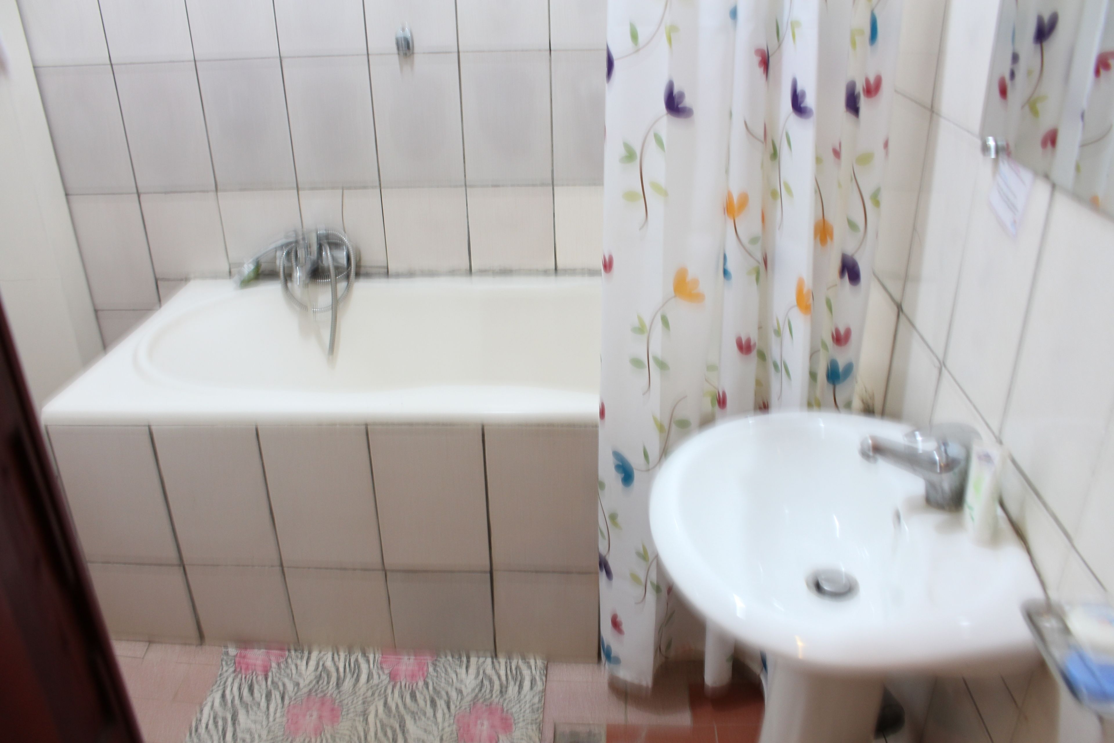 A bathroom with a bathtub, a sink, and a shower curtain with floral patterns.