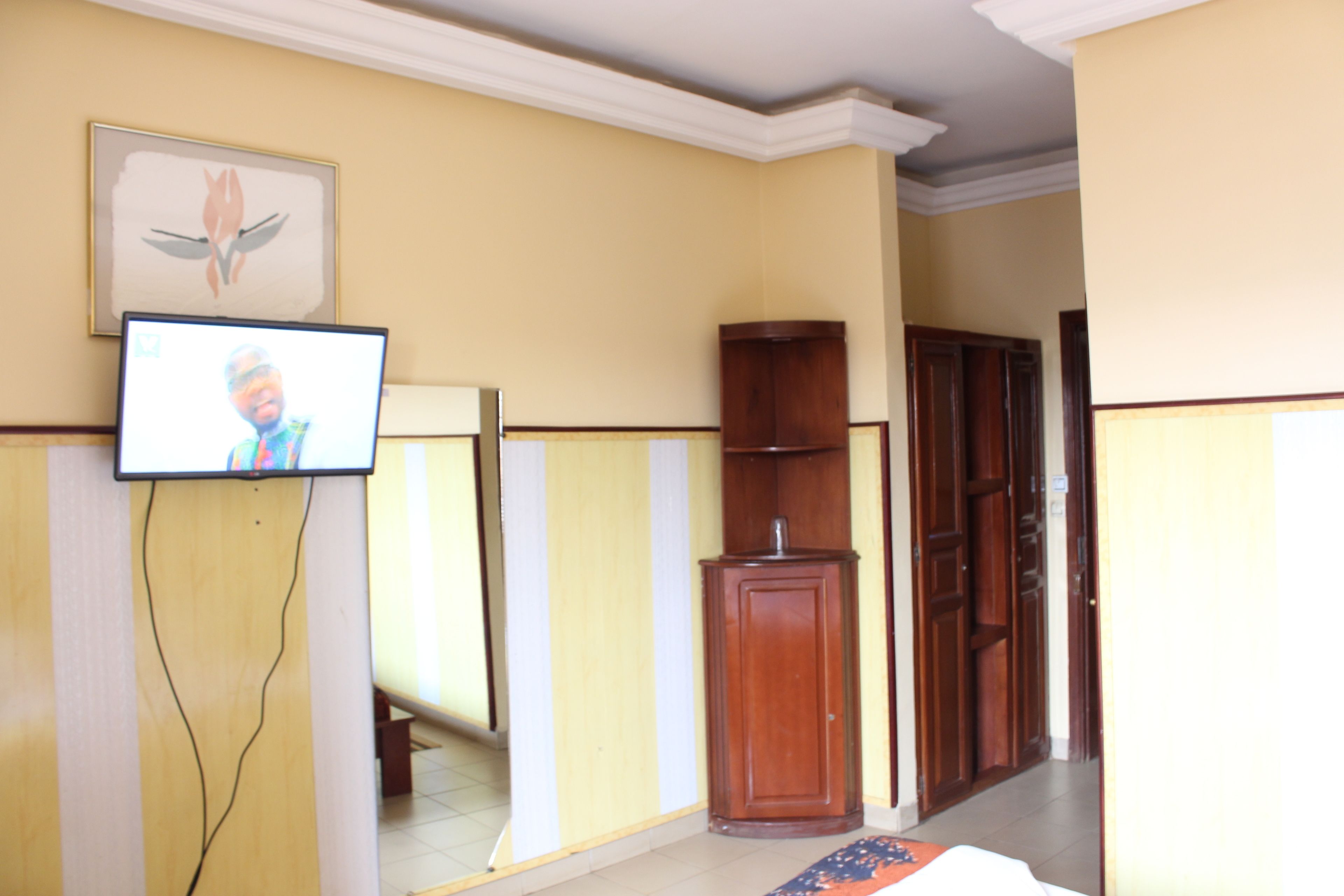 Ein Zimmer mit an der Wand montiertem Fernseher, einem Holzkasten und einer Tür zu einem anderen Raum.