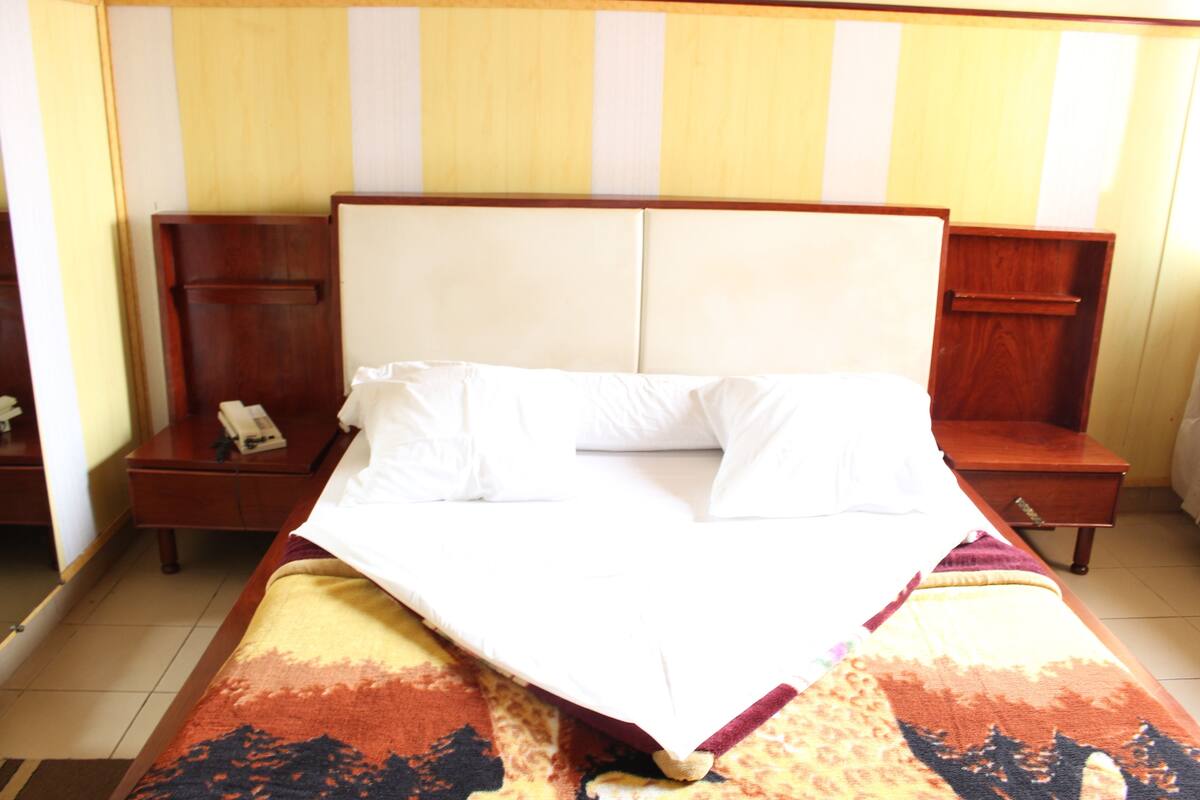 A hotel room with a large bed, wooden headboard, two bedside tables with lamps, and a striped wall.