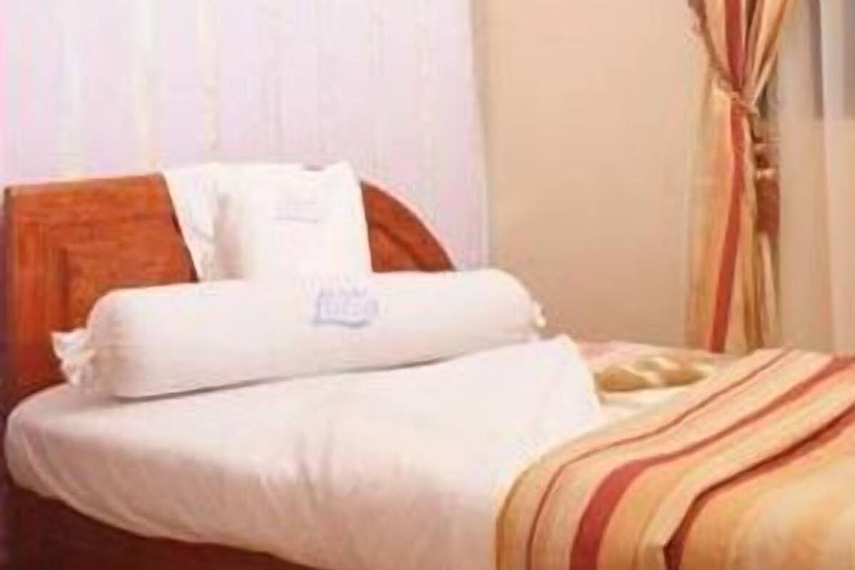 A hotel room with a wooden bed, white bedding, a window with curtains, and an air conditioning unit on the wall.