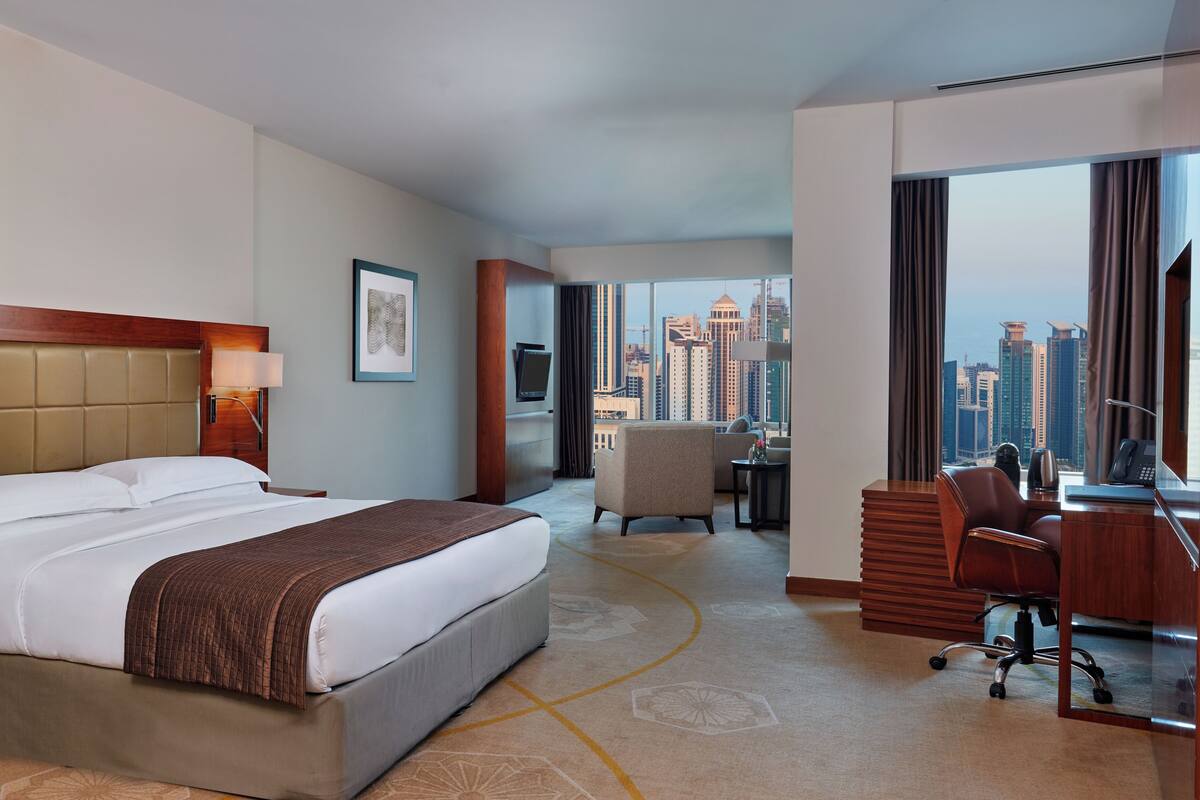 A hotel room with a large bed, a desk, a chair, a TV, and a city view.